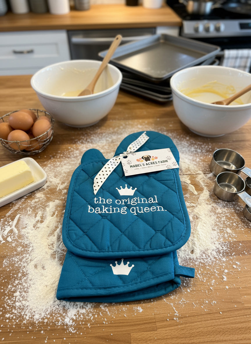 Blue oven mitt and pot holder set with 'the original baking queen' text on a textured surface.