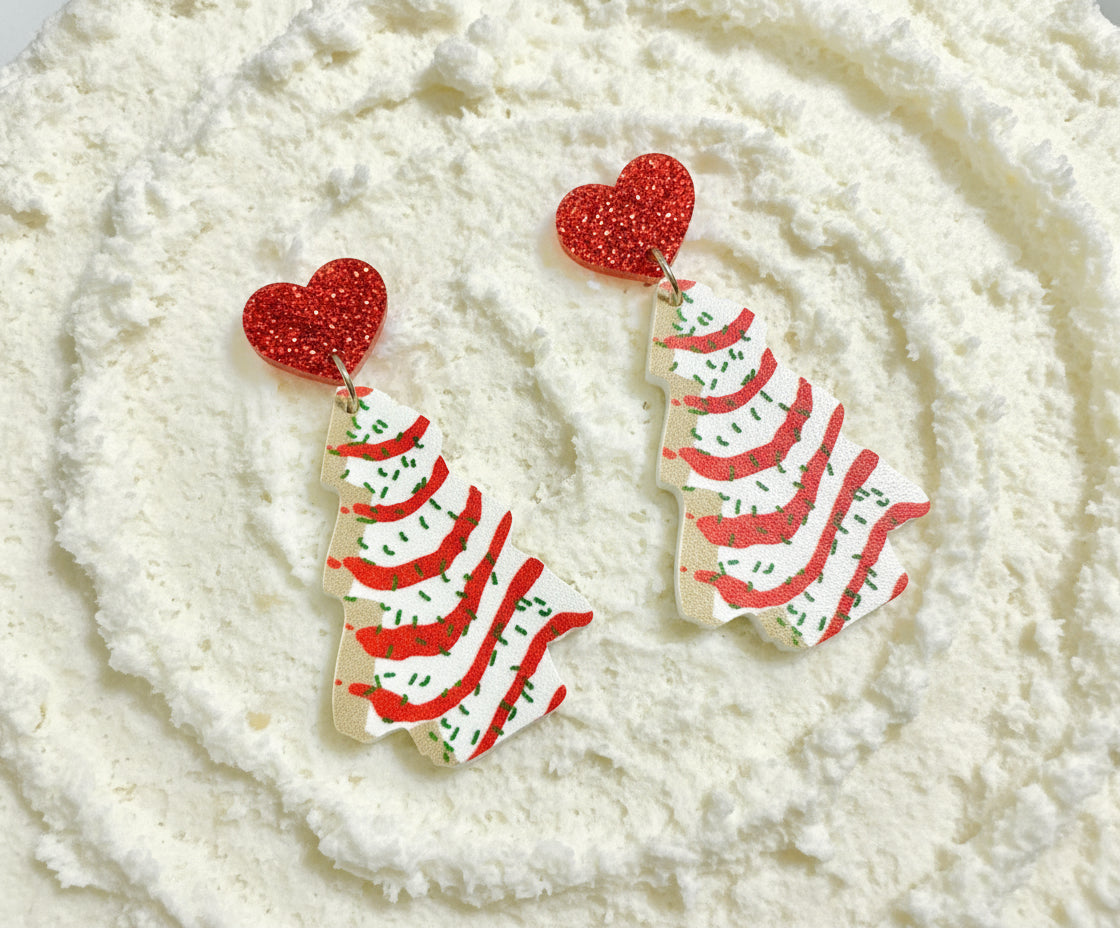 Christmas tree-shaped earrings with red glitter hearts on a white card with greenery.