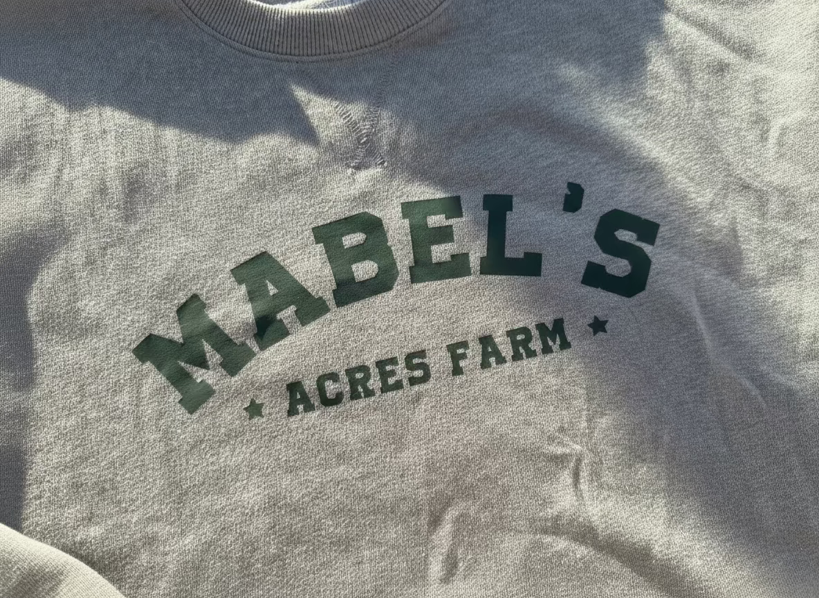 Gray sweatshirt with 'Mabel's Acres Farm' text in green on a textured fabric background