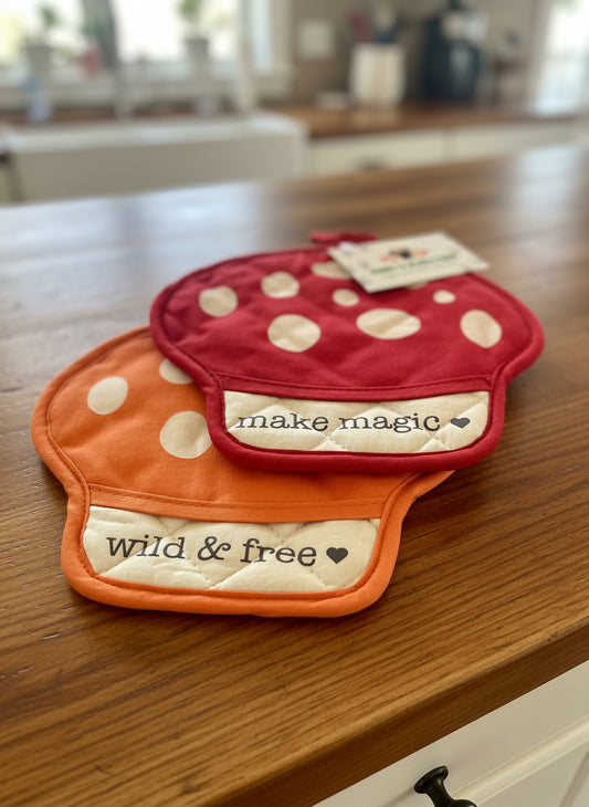 Two polka dot mushroom potholders with text on a textured surface, featuring a brand tag.